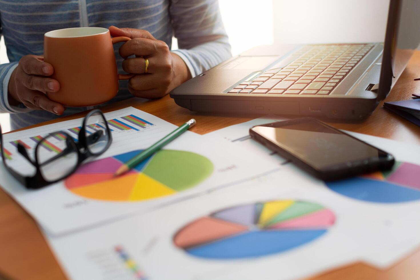 Woman holding a coffee cup with trade data chart document and laptop on working desk. photo