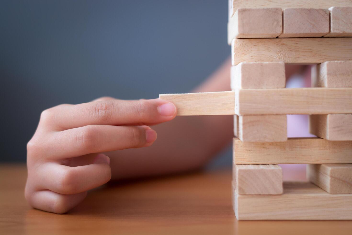 Hand of a girl placing and pulling wooden block on the tower. photo