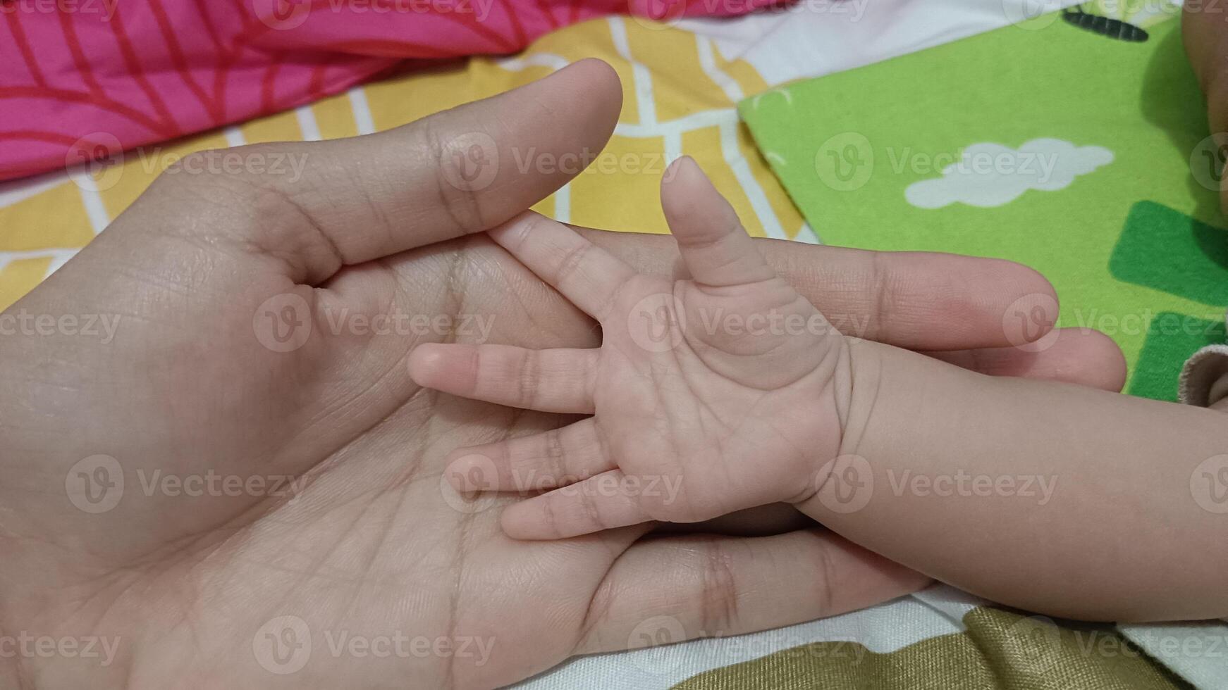 A mother's hand gently holds the tiny hand of her newborn baby. The image evokes a sense of love, care, and the bond between parent and child. photo