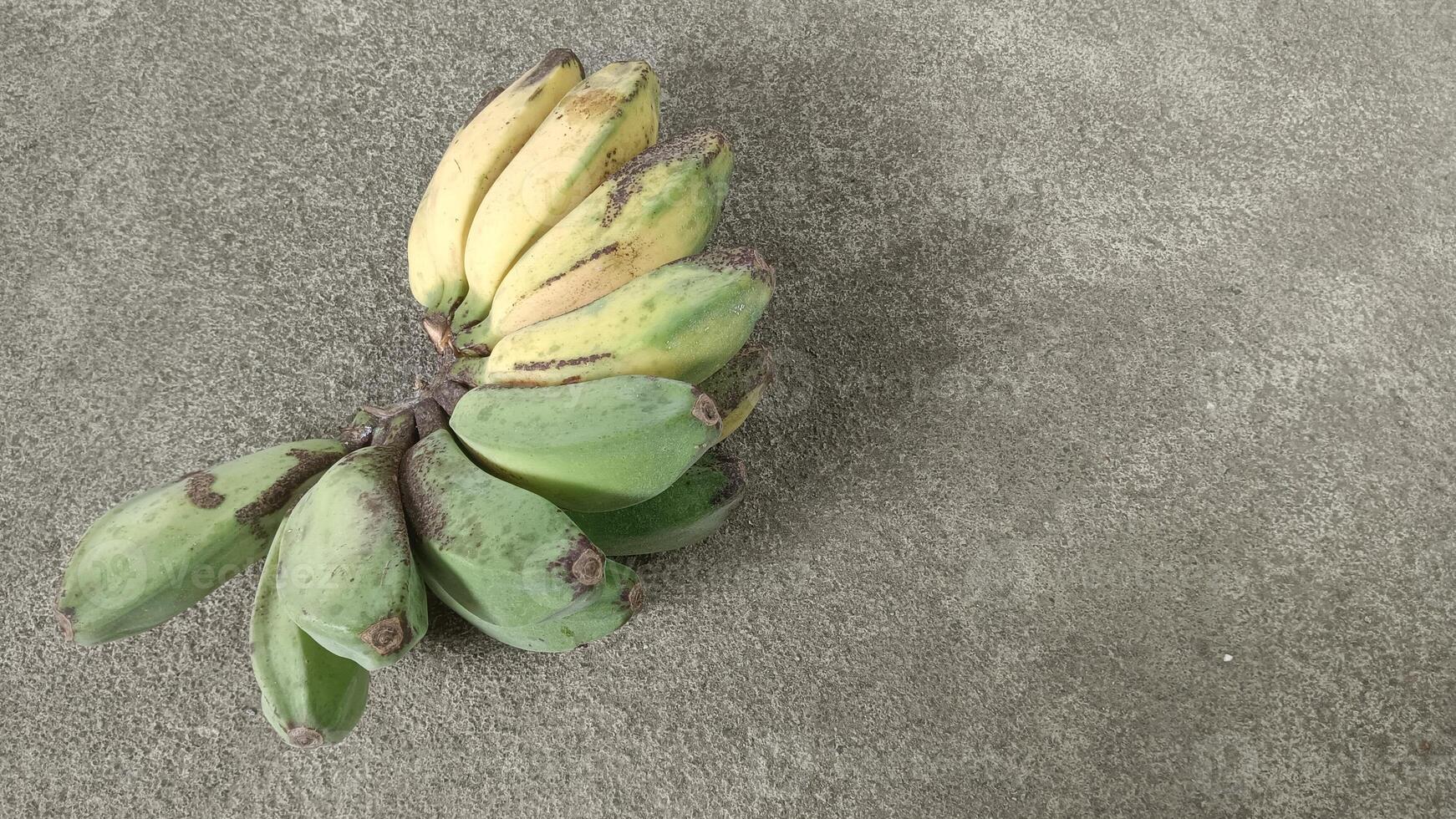 A bunch of ripe bananas with green and yellow peels on a grey concrete background. photo