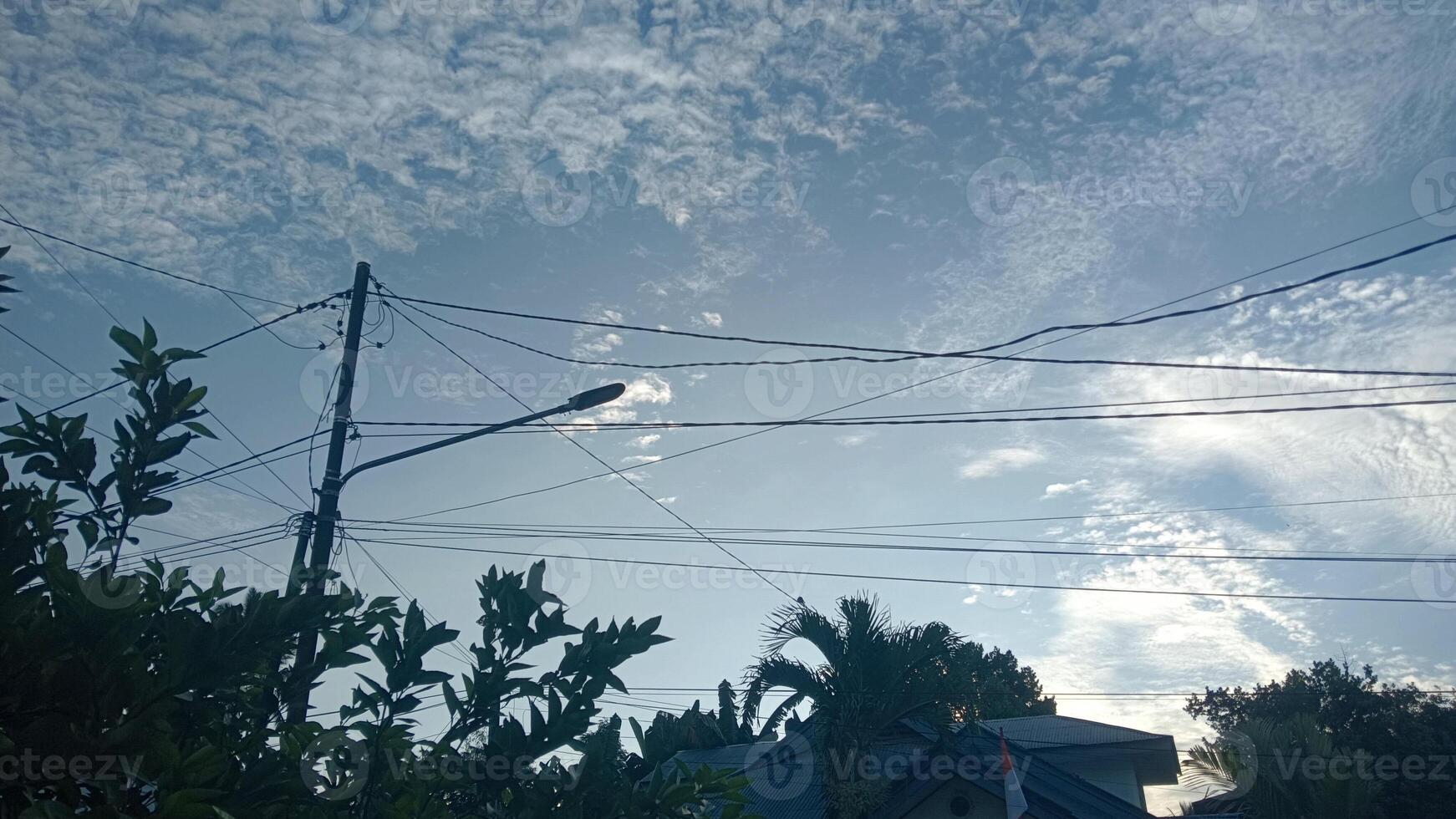 A blue sky with fluffy clouds and a streetlight with power lines. photo
