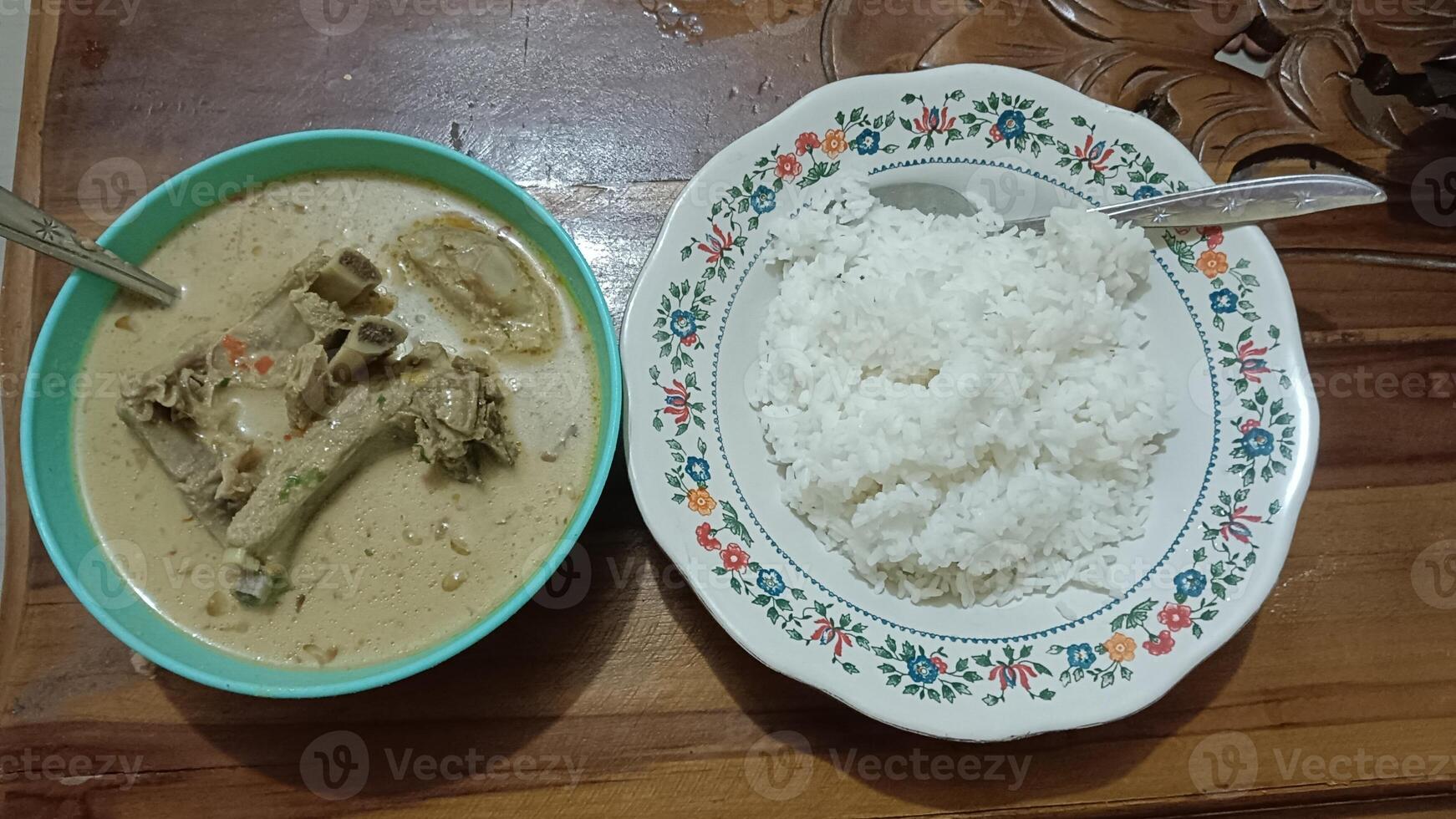 A bowl of white rice next to a bowl of soup with a spoon, served on a wooden table. photo