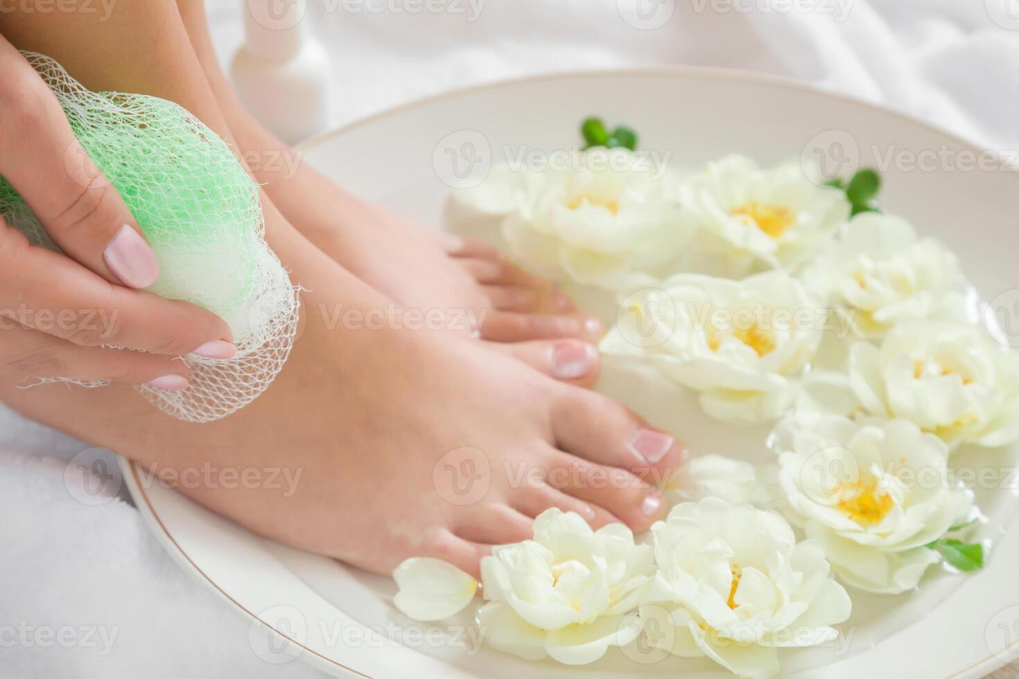 Woman washing her legs in the bow in the bathroom. Cares about a clean and soft skin with body creams, lotions or oils after shower and shaving. Fresh and fragrant white roses in the water. photo