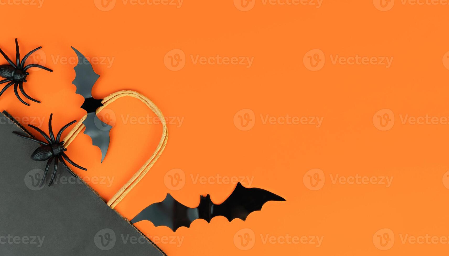 Flatlay composition with black bag, bats and spiders on orange background. Buying gifts for Halloween. Place for text. photo