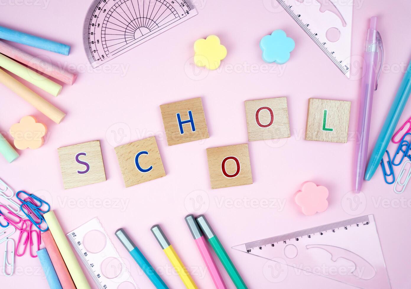 The letters Schooland school stationery lie on a pink background in the form of a frame. Top view. Back to school. photo
