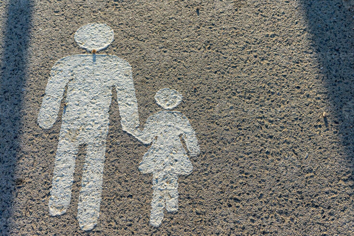 A painted ground image showing a man holding hands with a child, symbolizing a pedestrian walkway. The simple figures, in white, indicate safe crossing for pedestrians. photo