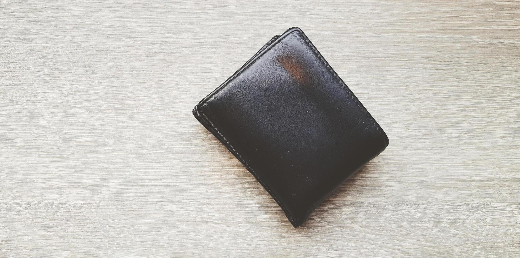 Black or brown leather wallet on light brown wooden table or background with copy space. Object, Money and Shape concept. photo