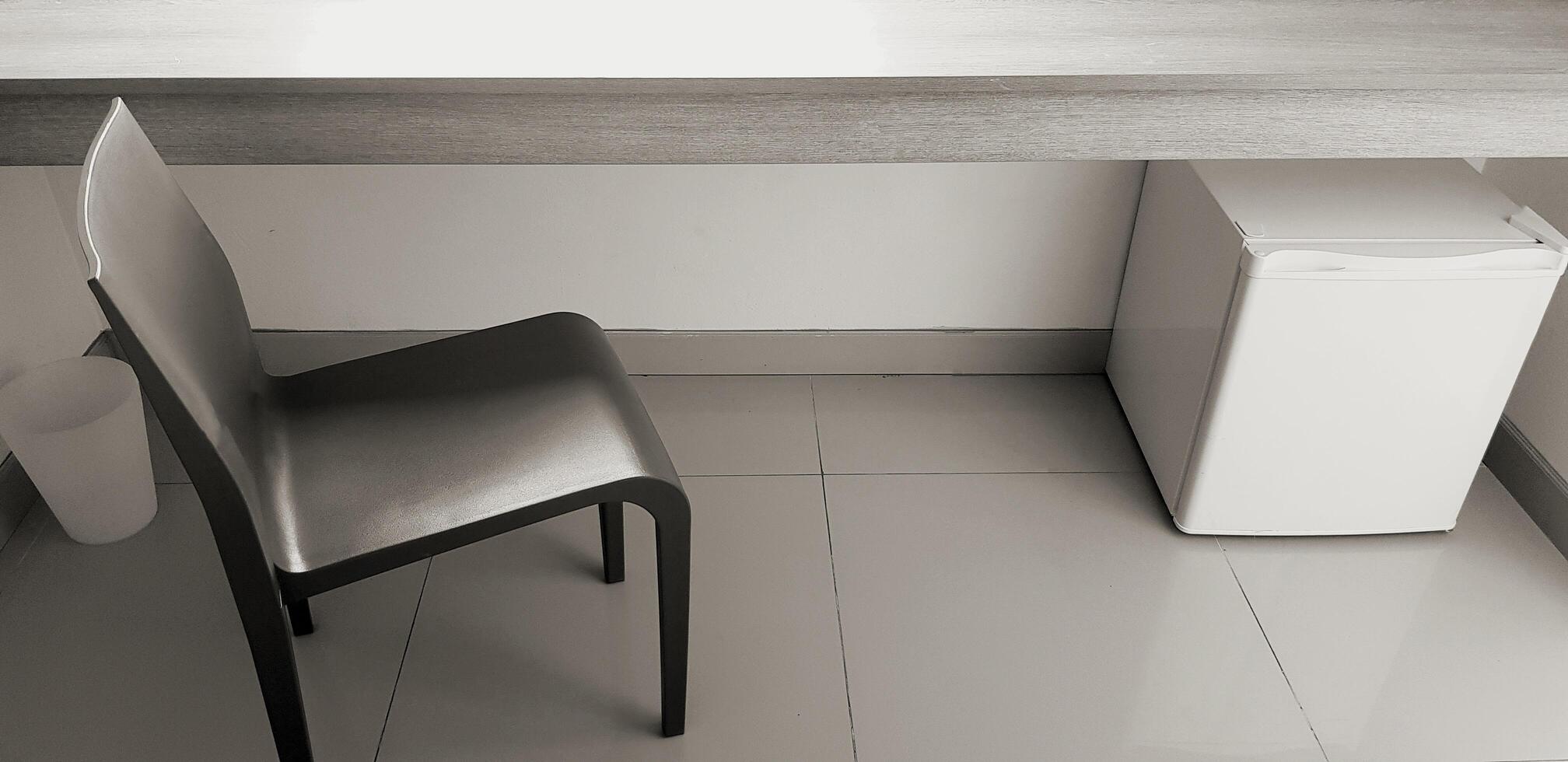Black chair with white refrigerator, white garbage putting on tile floor and wooden shelf in private room in monochrome style. Interior design and Modern furniture concept photo