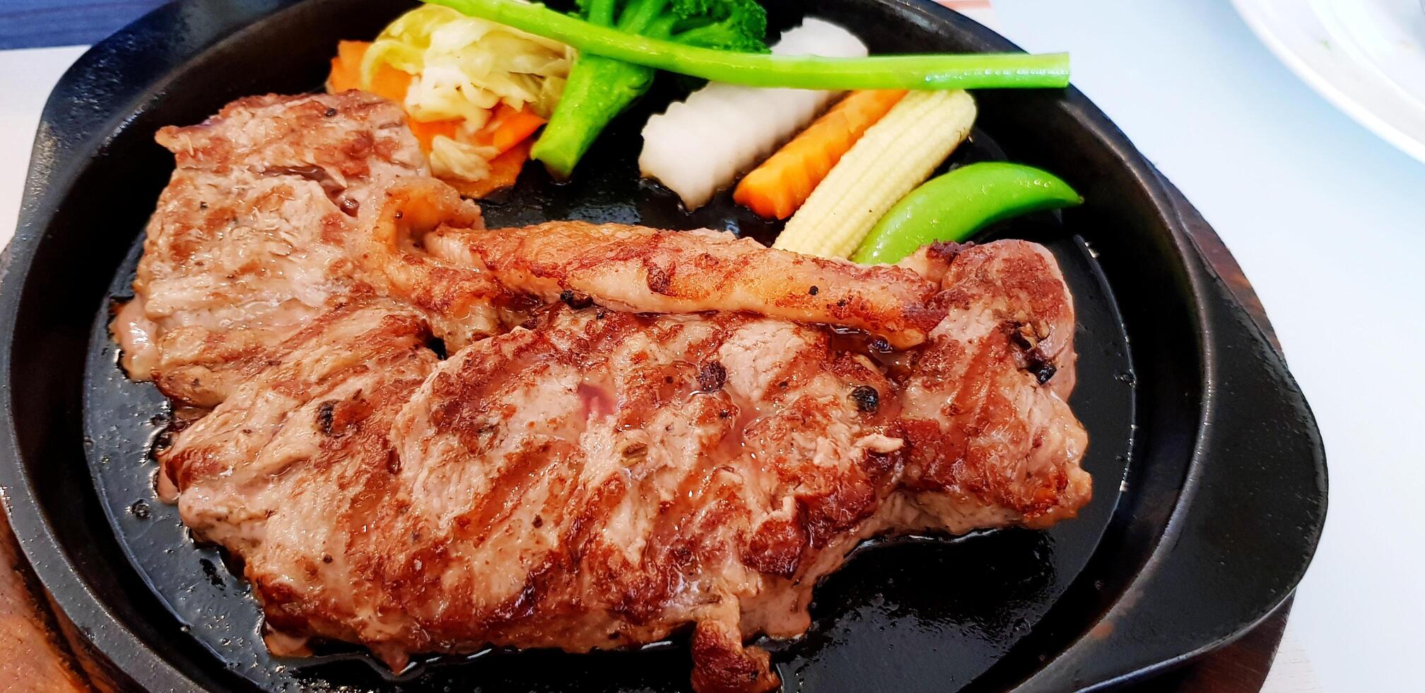 Close up tenderloin beef steak with vegetable, Green bean, carrot, broccoli and yellow corn sliced on hot black steel at restaurant. Premium food, photo