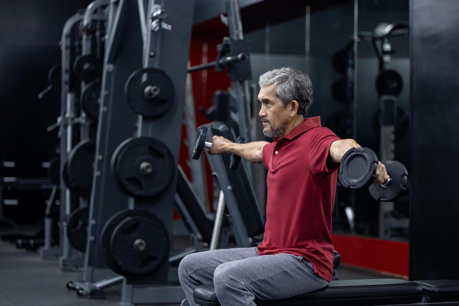 Asian senior man in sportswear doing weight lifting on double dumbbells to gain bicep muscle while having exercise training in the gym for longevity and retirement concept photo