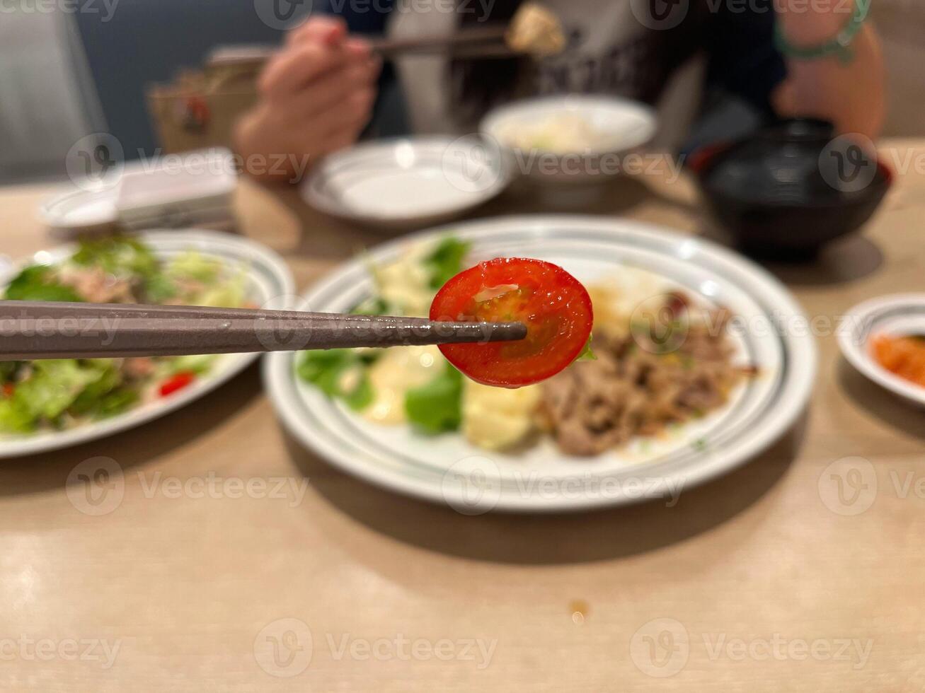 a chopstick is holding a slice of tomato with a blurred background of a meal, capturing the essence of a balanced and nutritious dining experience, Japanese meal photo