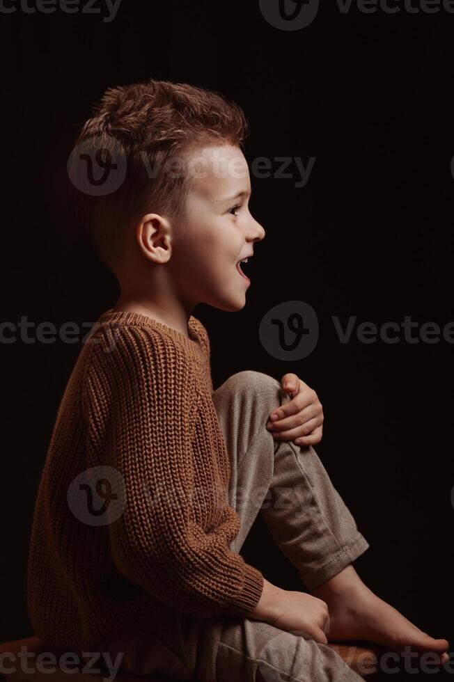 Profile portrait of a happy screaming stylish white Caucasian child preschooler kid boy on chair photo