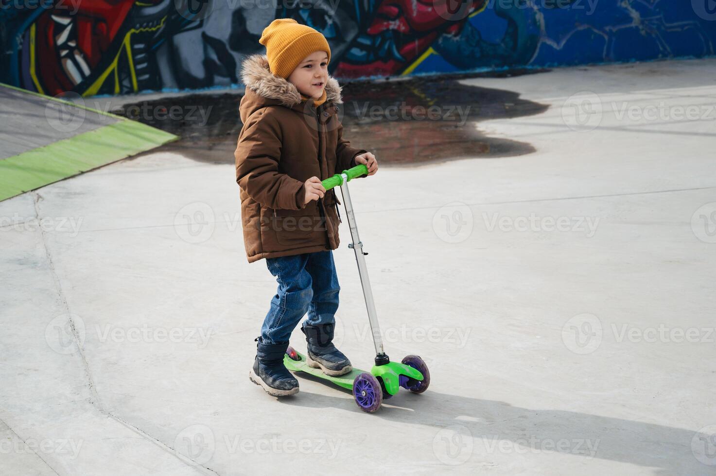 child preschooler kid boy rides a scooter in park on the playground in autumn photo