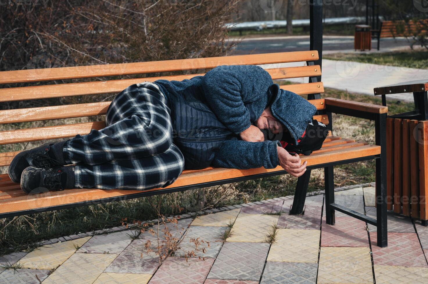 homeless dirty elderly old Caucasian man lies sleeping on park bench in autumn photo