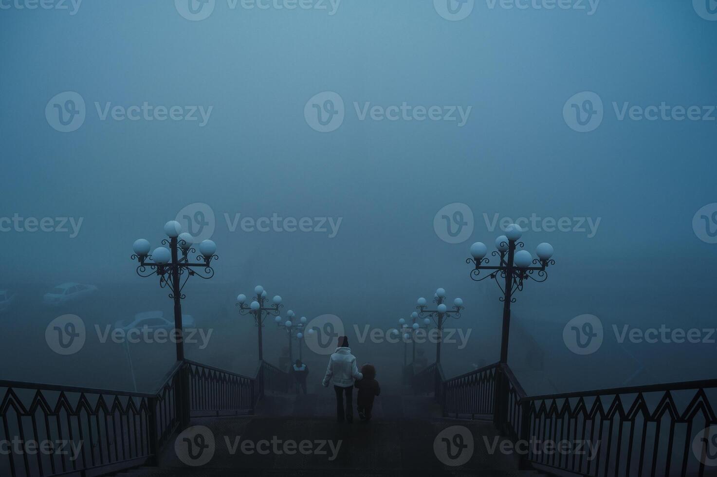 backs of a woman with a child boy going down the stairs on a foggy bridge in city on an autumn morning in fog mist photo