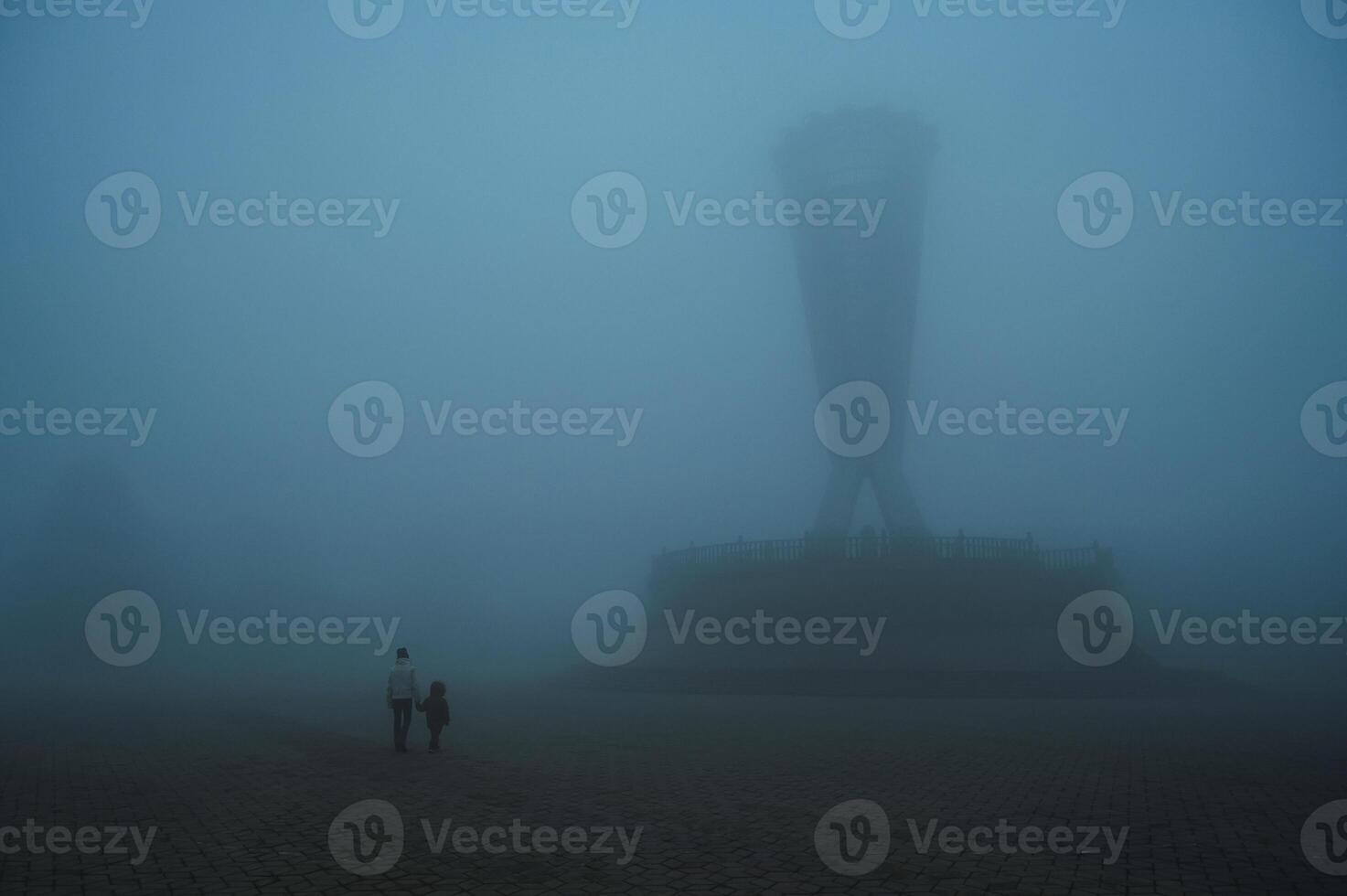 backs of mother woman with child son walking in a misty foggy mystical park in evening. A misty landscape with people in autumn in a misty fog mist haze photo