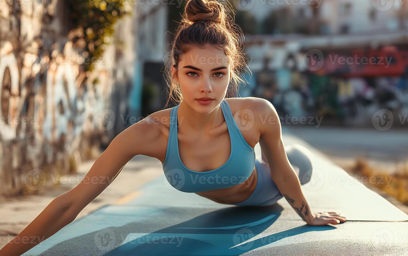 A beautiful woman with a bun in her hair does a push up on a blue yoga mat in a city environment. photo
