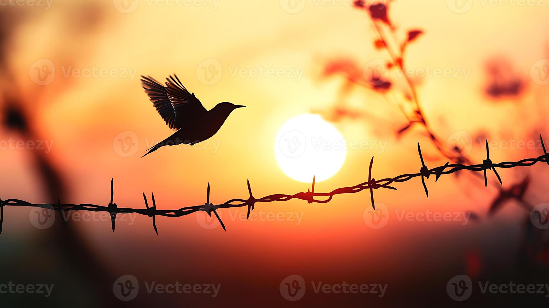 A bird takes flight over barbed wire fence as the sun sets, creating a silhouette against the vibrant orange sky. photo