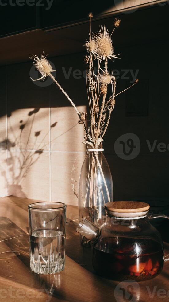 A glass in the shade is a hot drink with a glass teapot of strong tea on a wooden table under sunlight photo