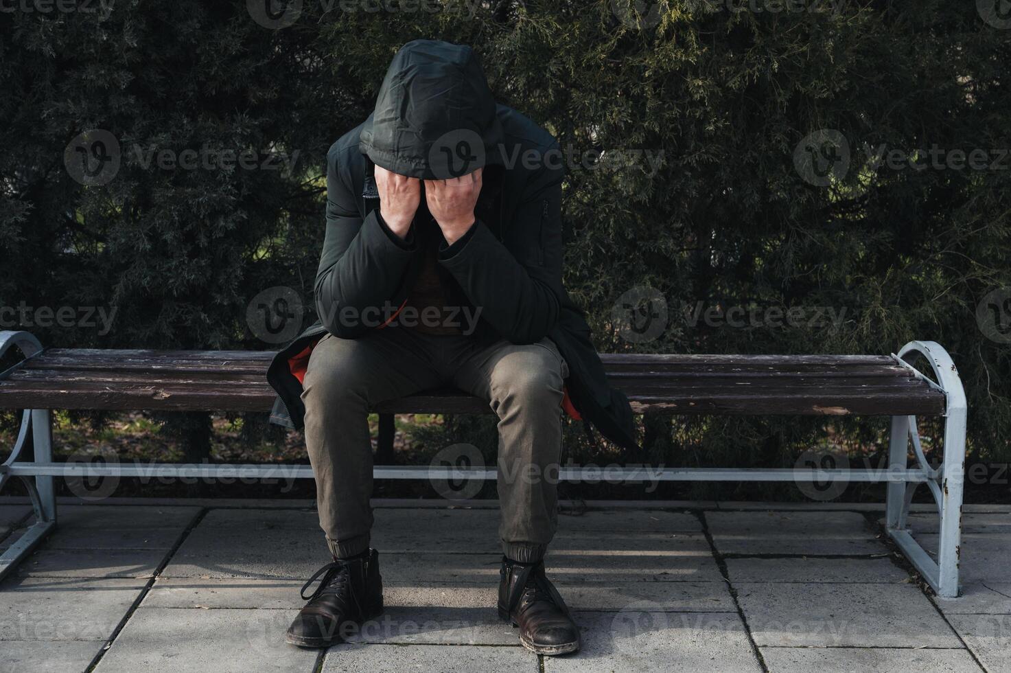 sad lonely man homeless depressed and upset sits on park bench and covers his face with his hands photo