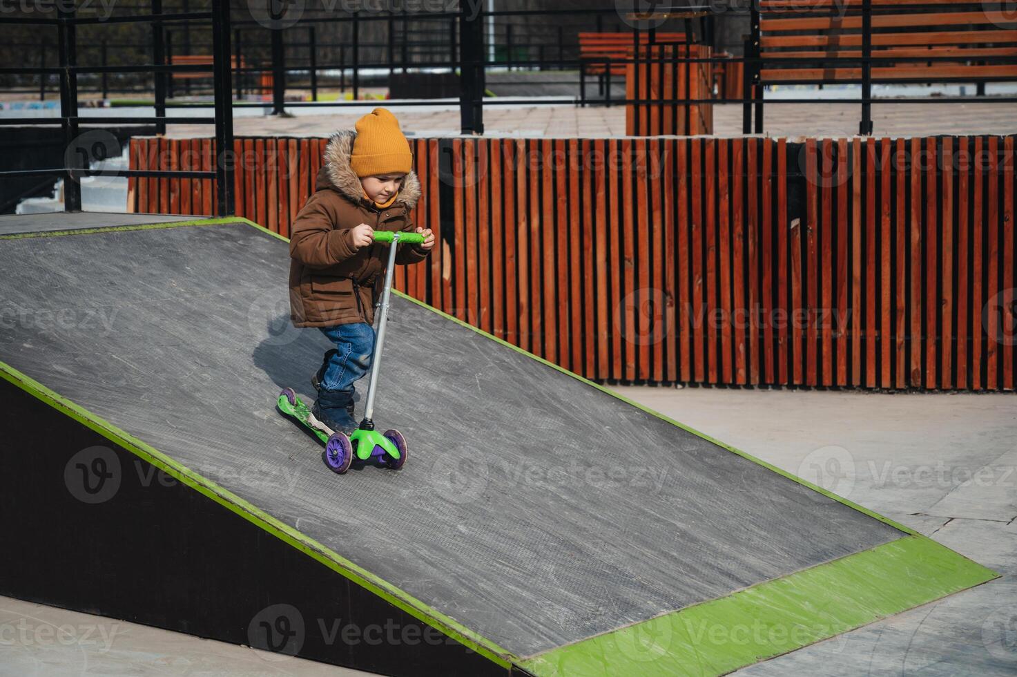 child preschooler kid boy rides a scooter in park on a skateboard ramp in the autumn photo