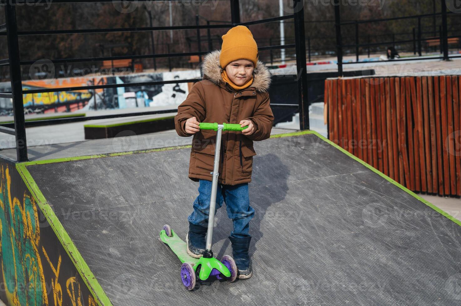 child preschooler kid boy rides a scooter in park on a skateboard ramp in the autumn photo