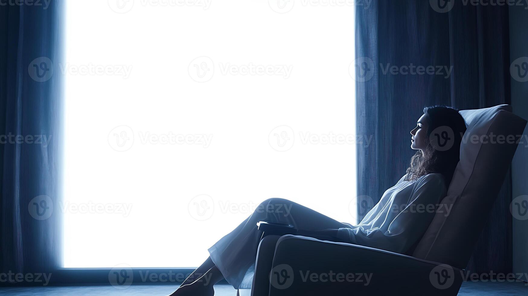 Woman relaxing in a comfortable armchair, looking out a large window. photo