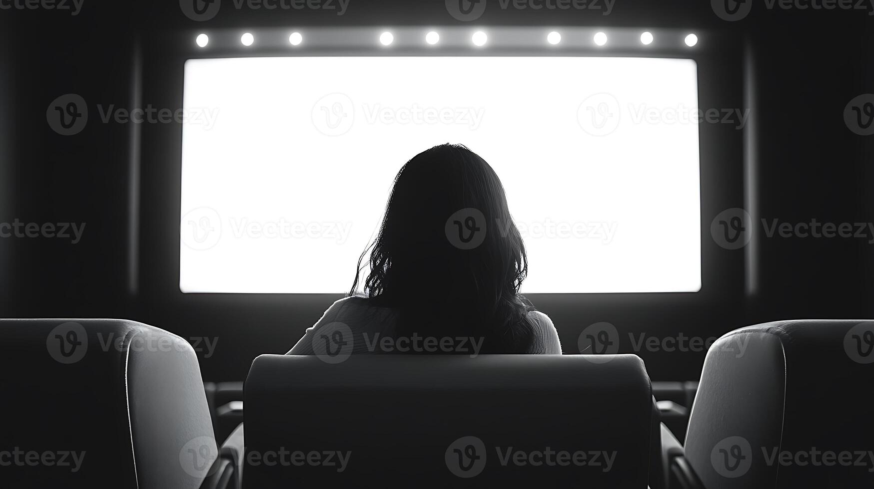 Woman watching a movie in a dark theater with a blank screen. photo