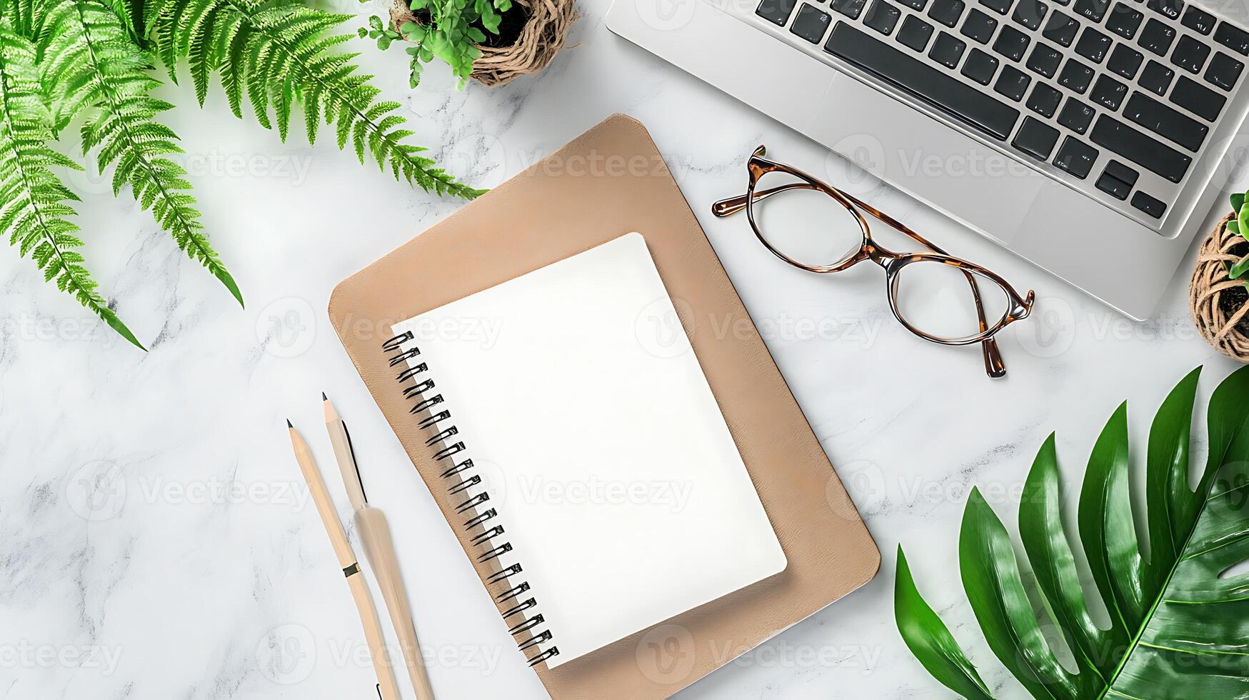 Top view of a white marble table with a notebook, pencils, laptop, glasses, and greenery. photo