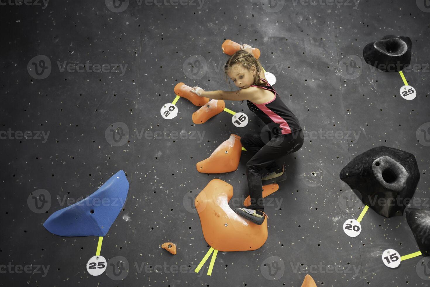 Sporty little girl climbing artificial wall with grips at club photo