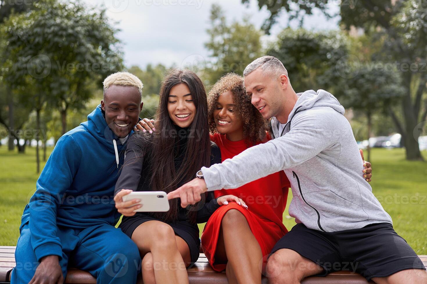 Happy diverse friends taking selfie using smartphone in park photo