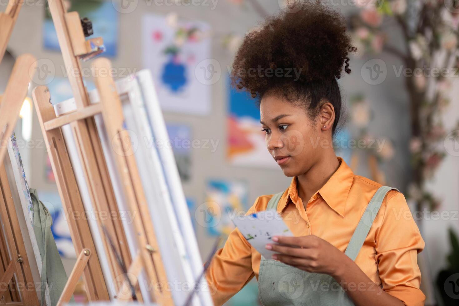 Young Girl Drawing in a Painting Studio with Colorful Artwork and Canvases in the Background, Wearing an Apron and Concentrating on Her Work photo