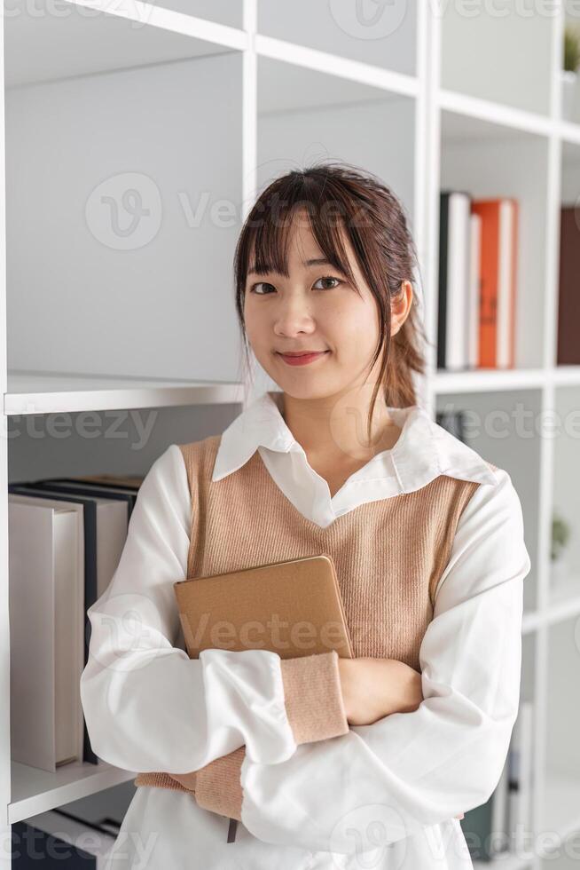 Confident Young Female Office Worker Holding Notebook in Modern Workspace with Shelves and Books photo