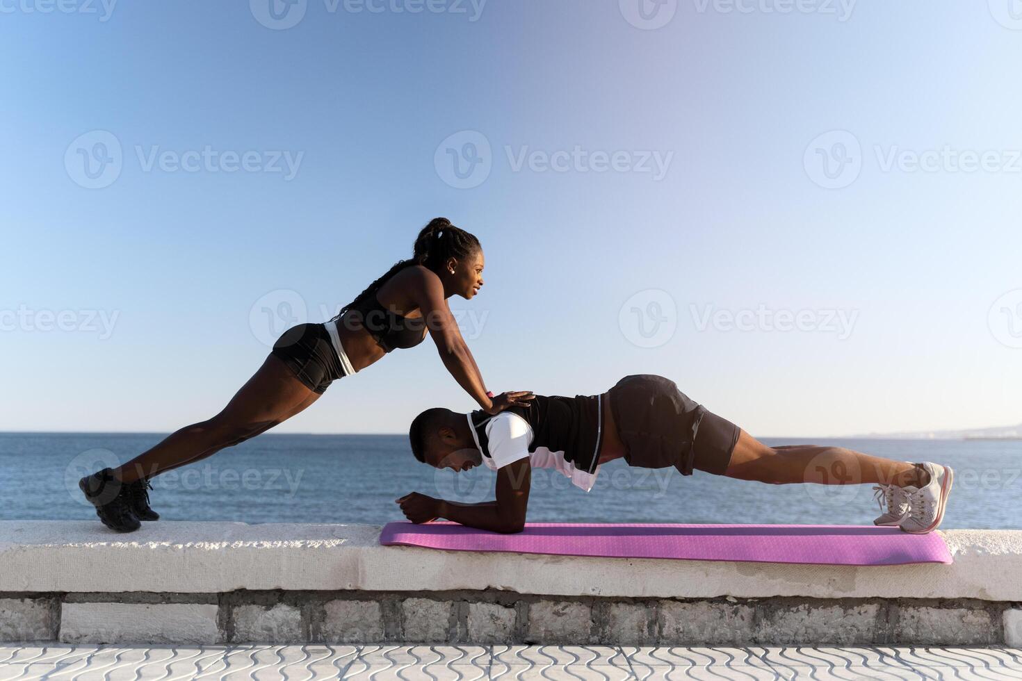 Multiracial young cheerful couple making plank exercise while having workout photo
