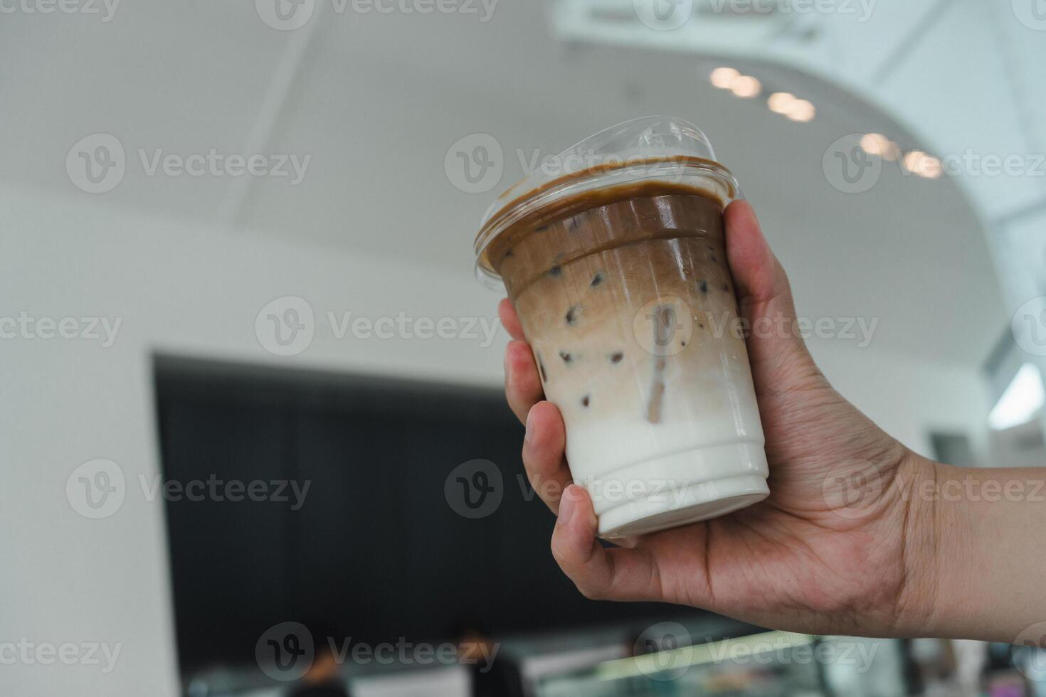 Cropped shot view of someone hand holding a plastic cup of Iced latte coffee photo
