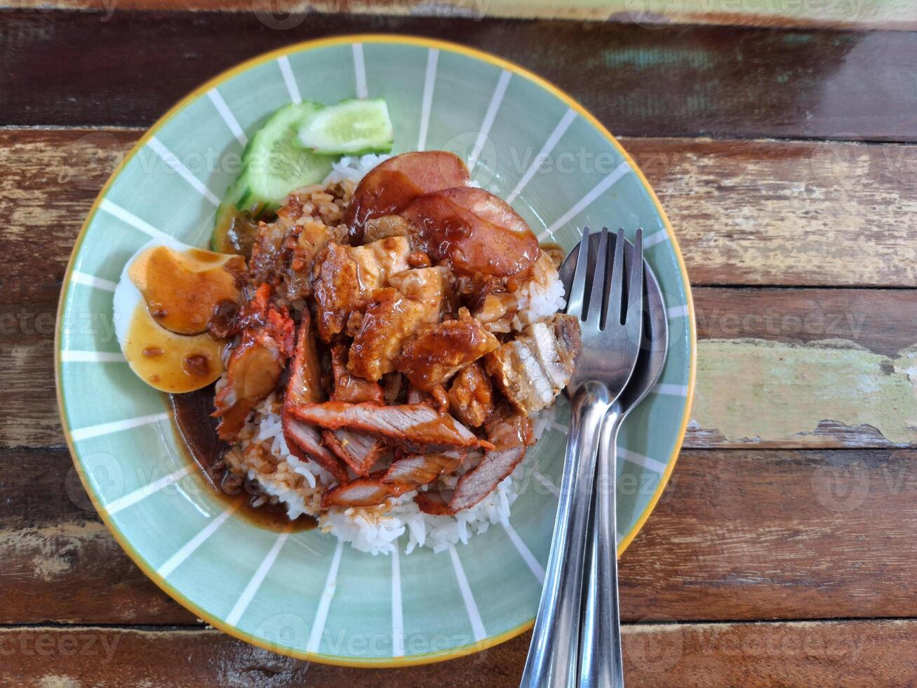 photo of food on a plate placed on a wooden table ,Roast pork rice