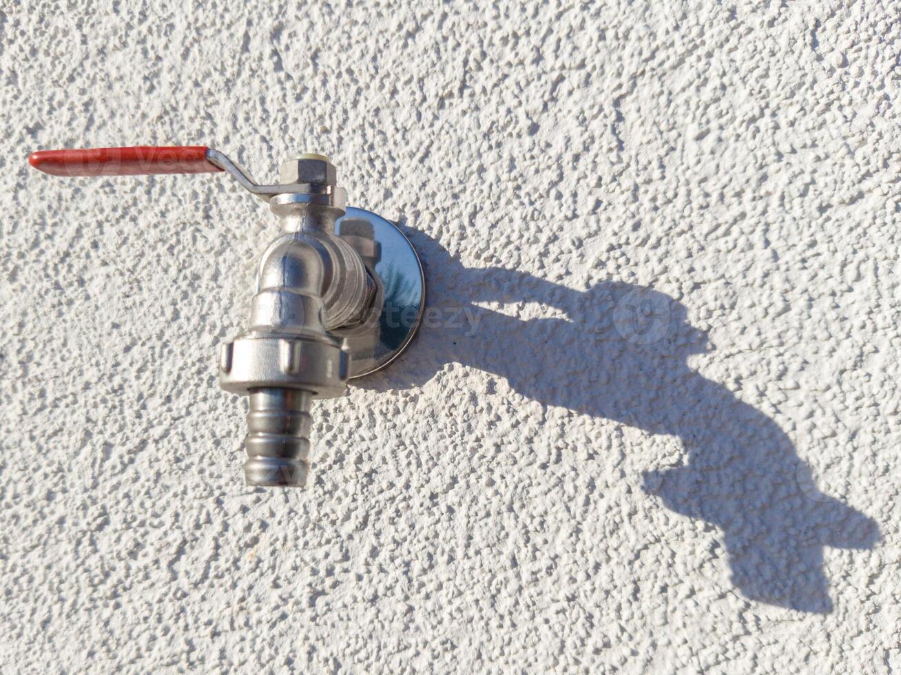 Outdoor Water Faucet with Red Handle Casting Shadow photo