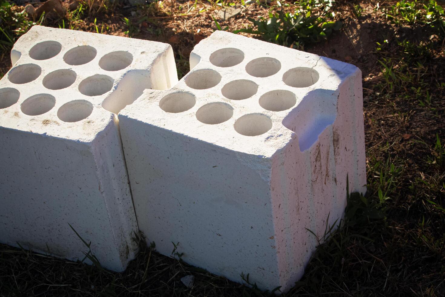 Two cubical white bricks with round holes lying on the ground under sunlight in summer photo