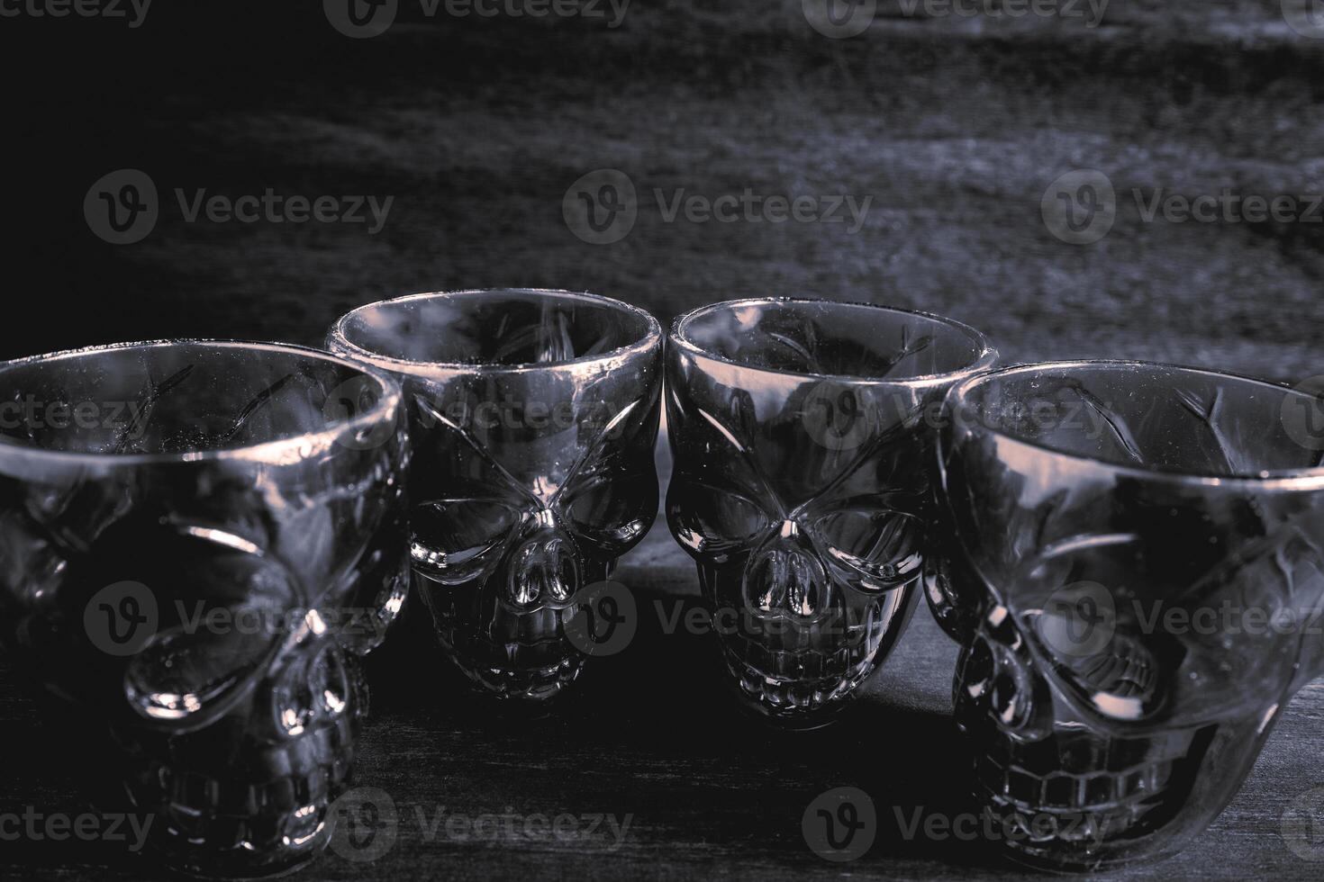 A couple of shot glasses in the shape of a skull, for a Halloween Party. On a wooden background, in black and white. photo