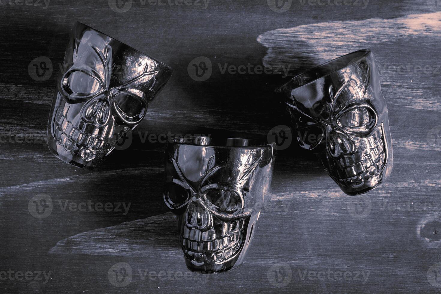 A couple of shot glasses in the shape of a skull, for a Halloween Party. On a wooden background, in black and white. photo