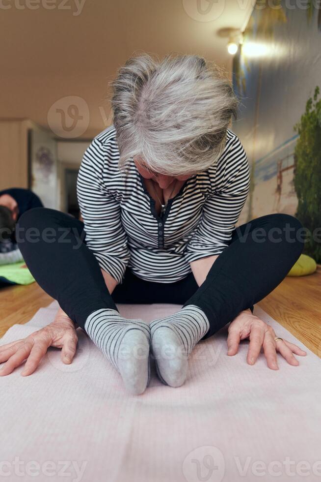 A group of senior women engage in various yoga exercises, including neck, back, and leg stretches, under the guidance of a trainer in a sunlit space, promoting well-being and harmony photo