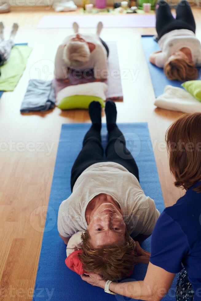 Top view of group of senior women engage in various yoga exercises, including neck, back, and leg stretches, under the guidance of a trainer in a sunlit space, promoting well-being and harmony photo