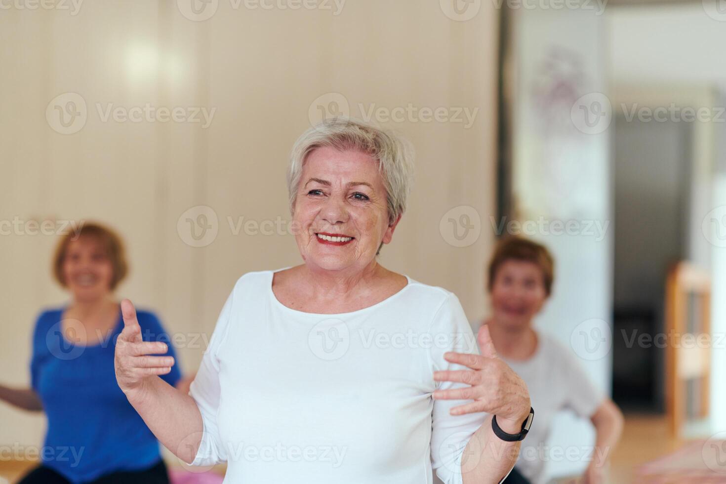 A group of senior women engage in various yoga exercises, including neck, back, and leg stretches, under the guidance of a trainer in a sunlit space, promoting well-being and harmony photo
