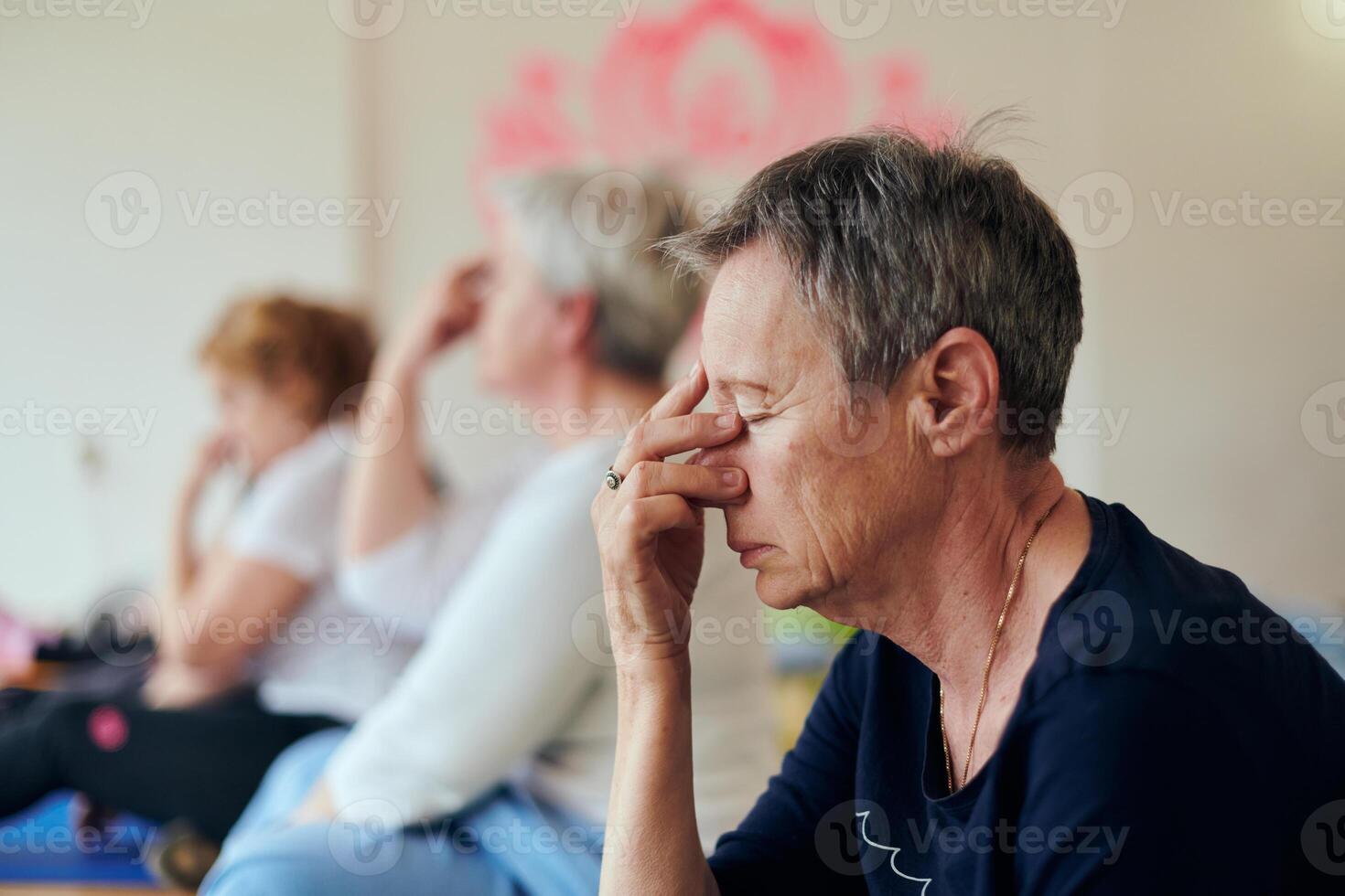 A group of senior women engage in various yoga exercises, including neck, back, and leg stretches, under the guidance of a trainer in a sunlit space, promoting well-being and harmony photo