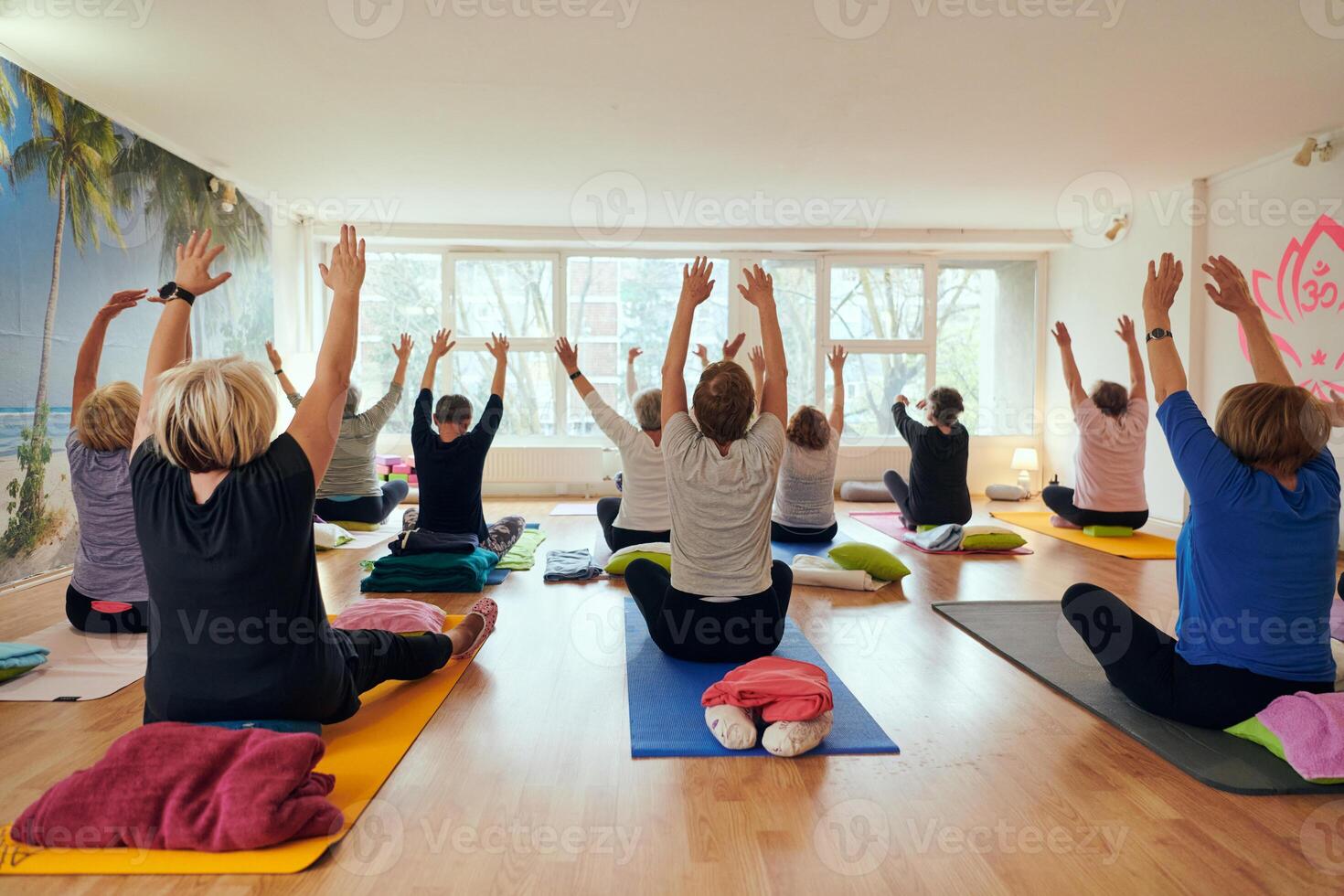 A group of senior women engage in various yoga exercises, including neck, back, and leg stretches, under the guidance of a trainer in a sunlit space, promoting well-being and harmony photo