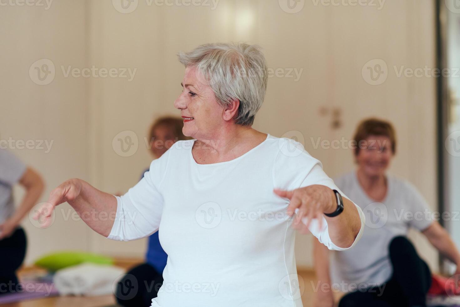 A group of senior women engage in various yoga exercises, including neck, back, and leg stretches, under the guidance of a trainer in a sunlit space, promoting well-being and harmony photo