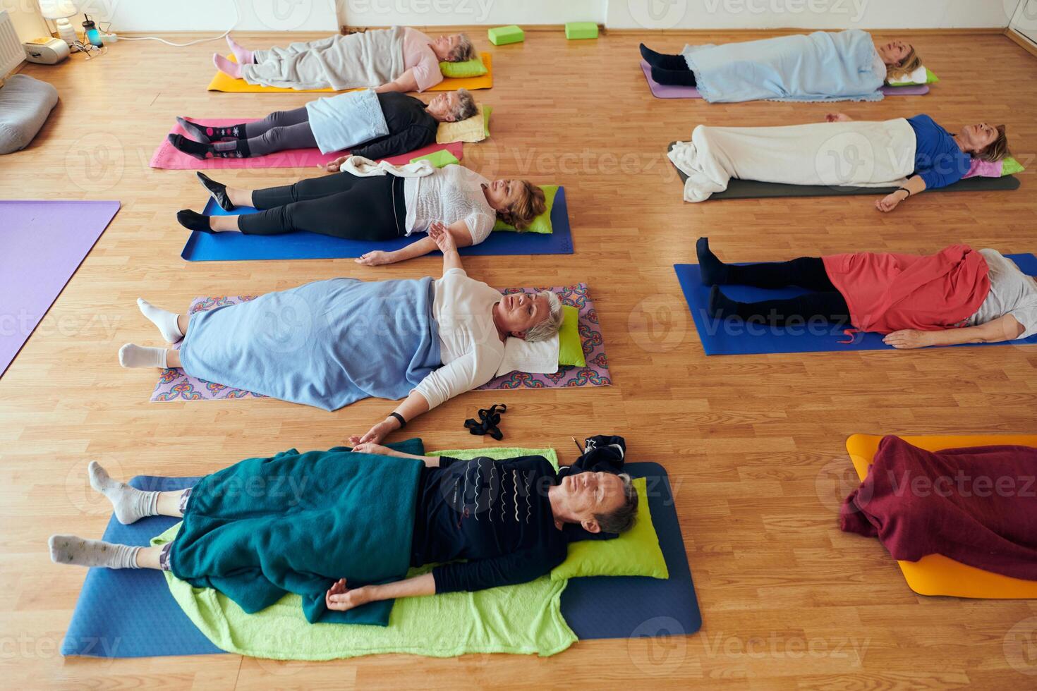 A group of senior women engage in various yoga exercises, including neck, back, and leg stretches, under the guidance of a trainer in a sunlit space, promoting well-being and harmony photo