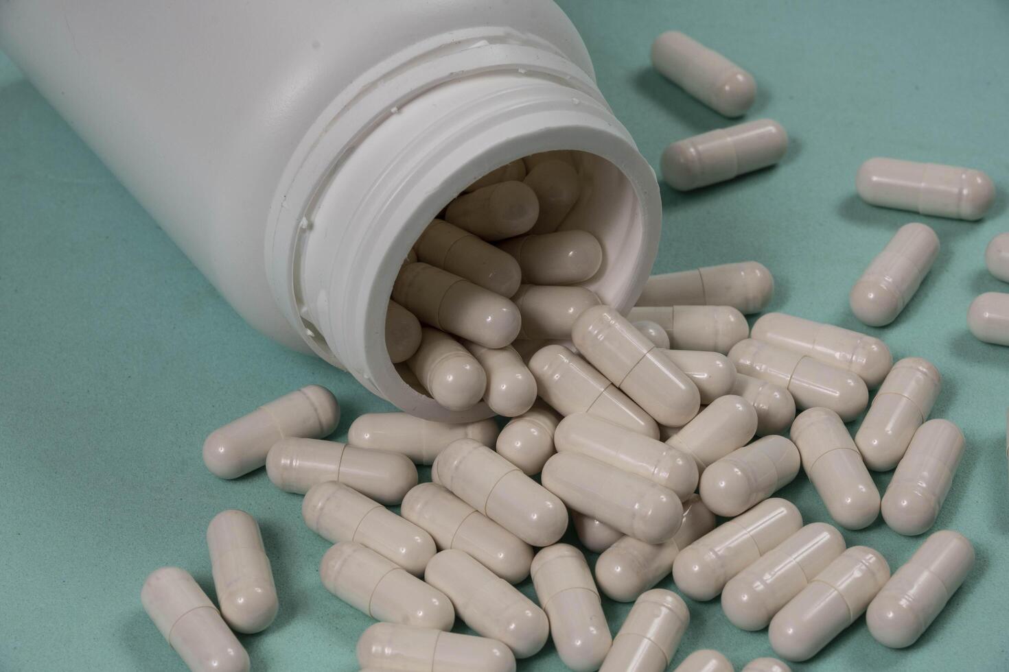 bottle of pills, some of which spilled onto a light blue surface photo