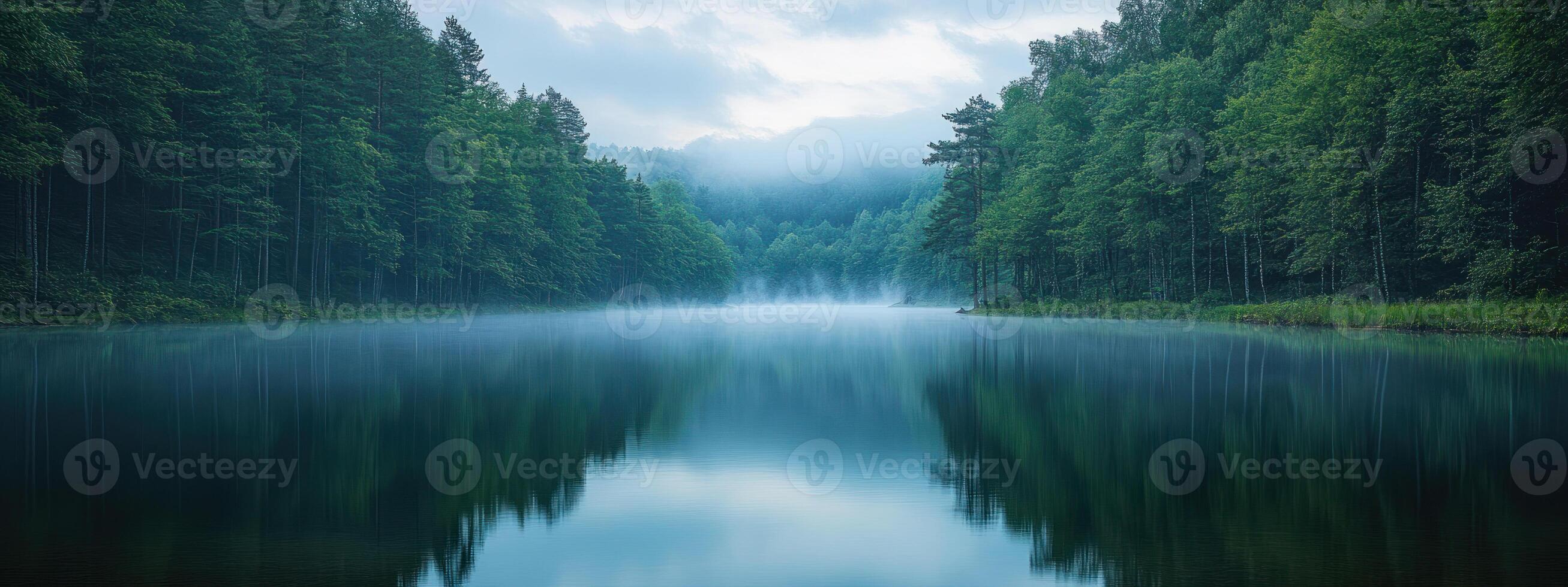 A serene shot of lake surrounded by dense forest, reflecting calmness of nature. mist adds tranquil atmosphere to scene. photo