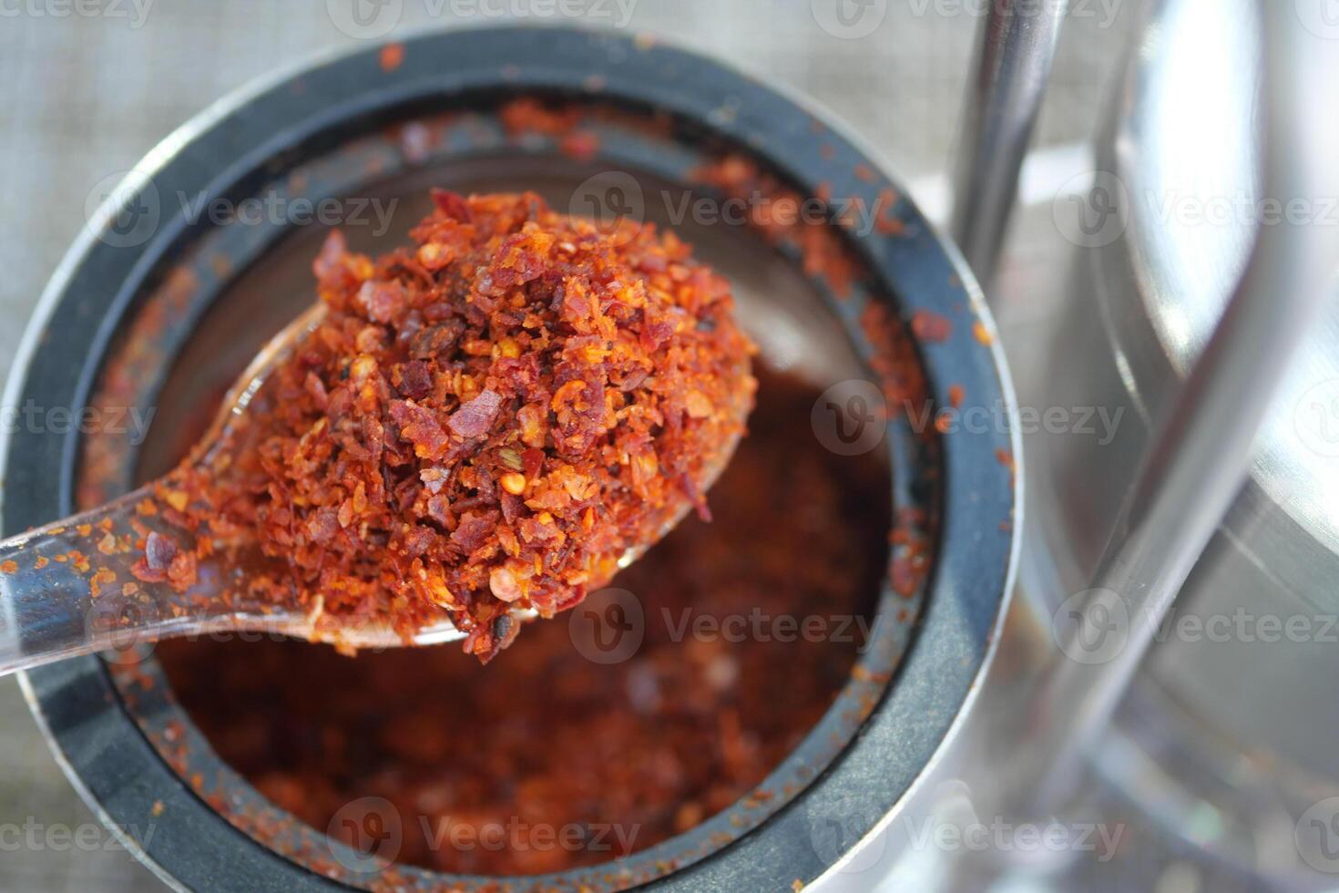A Detailed CloseUp of Vibrant Red Chili Flakes in a Spoon Arranged atop a Spice Container photo